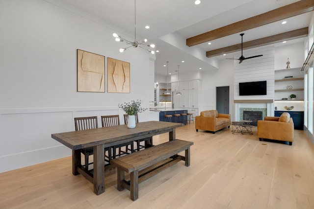 dining space with light wood-type flooring, ceiling fan with notable chandelier, a fireplace, and beam ceiling