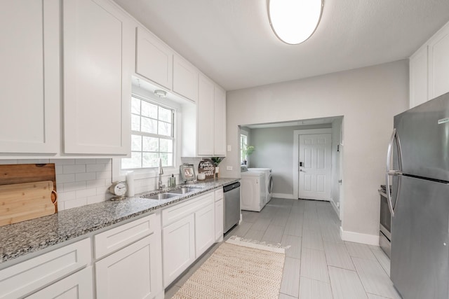 kitchen with white cabinets, sink, light stone counters, stainless steel appliances, and washing machine and clothes dryer