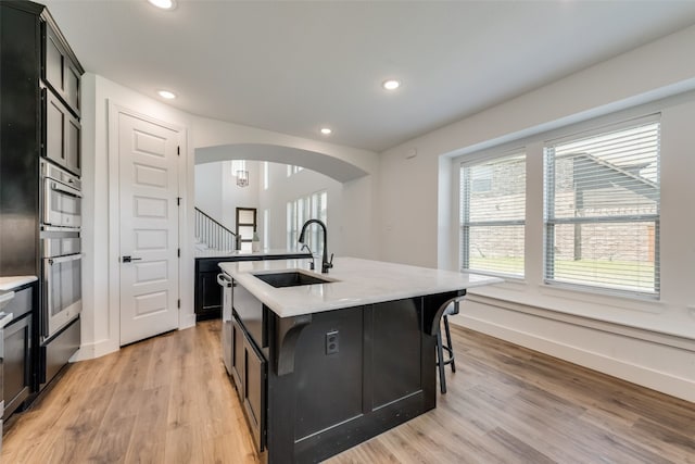 kitchen with sink, light wood-type flooring, stainless steel oven, and an island with sink