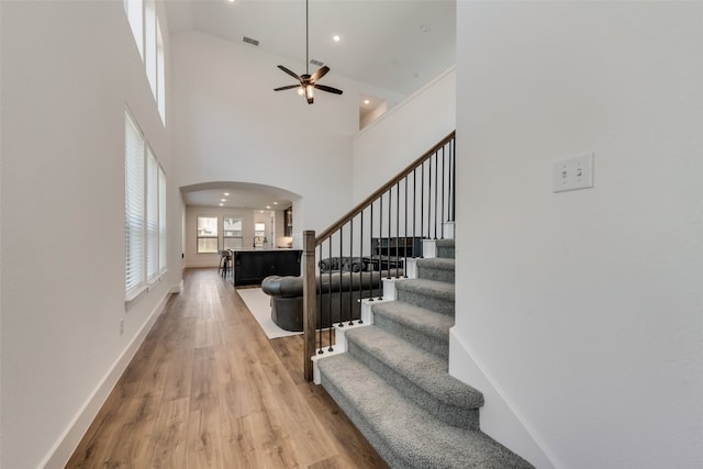 stairway with ceiling fan, light hardwood / wood-style floors, and a high ceiling