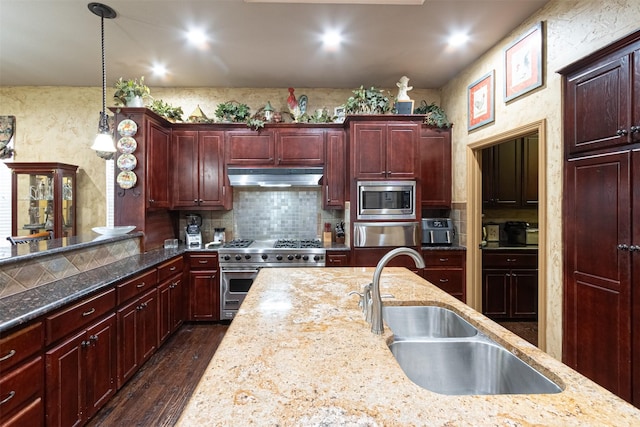 kitchen with appliances with stainless steel finishes, decorative light fixtures, dark wood-type flooring, sink, and light stone counters