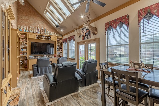 living room with a skylight, light hardwood / wood-style floors, ceiling fan, ornamental molding, and high vaulted ceiling