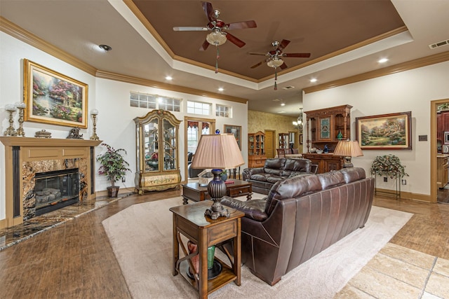 living room with a fireplace, ceiling fan, a tray ceiling, light hardwood / wood-style flooring, and crown molding