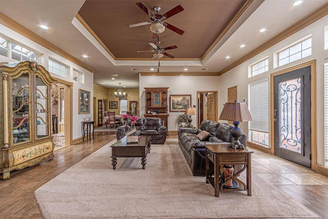 living room featuring ornamental molding, ceiling fan with notable chandelier, and a tray ceiling