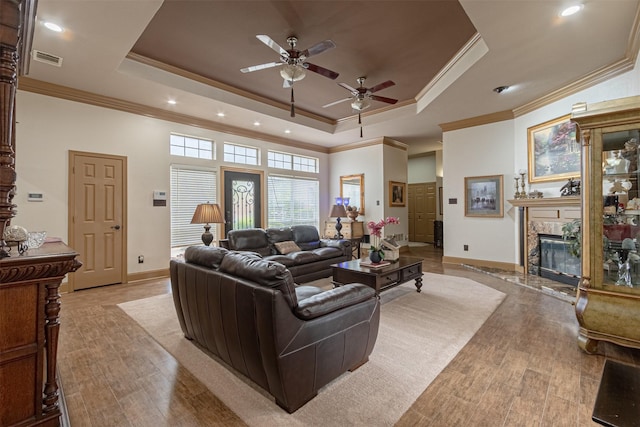 living room with ceiling fan, a high end fireplace, light hardwood / wood-style floors, and a raised ceiling