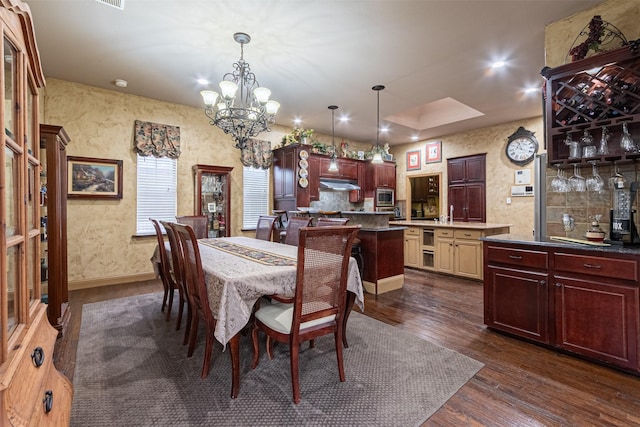 dining space with dark wood-type flooring, an inviting chandelier, and a tray ceiling