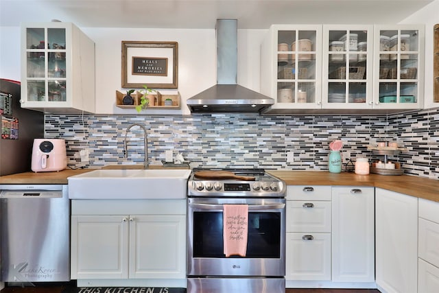 kitchen with wood counters, stainless steel appliances, wall chimney exhaust hood, sink, and tasteful backsplash