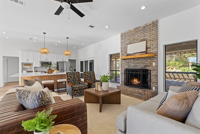 living room with ceiling fan, sink, light wood-type flooring, and a fireplace