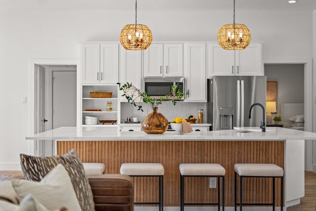 kitchen with white cabinets, an island with sink, stainless steel appliances, and wood-type flooring