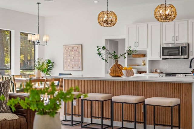 kitchen with a kitchen bar, tasteful backsplash, pendant lighting, a chandelier, and white cabinetry