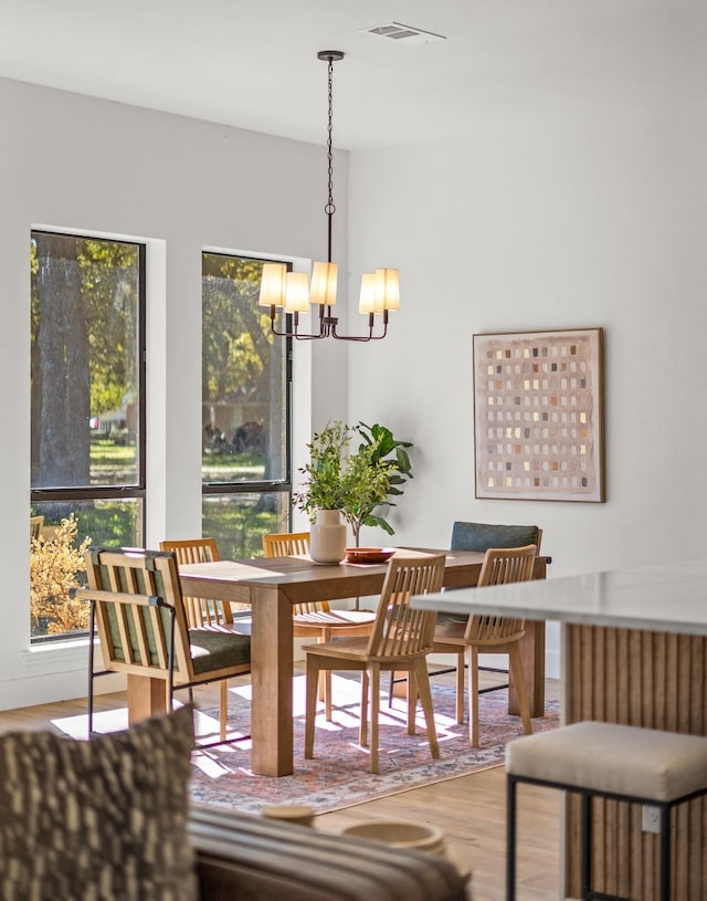 dining area with wood-type flooring, a healthy amount of sunlight, and an inviting chandelier