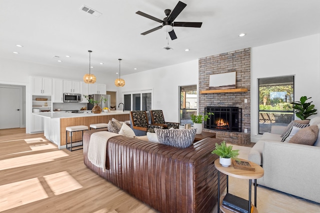 living room featuring a brick fireplace, ceiling fan, and light wood-type flooring