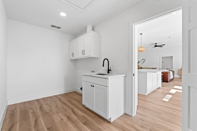 interior space with a breakfast bar, ceiling fan, sink, white cabinets, and light hardwood / wood-style floors