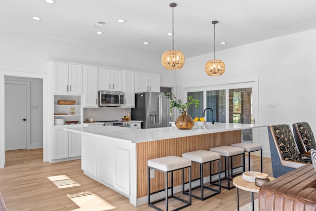 kitchen featuring a large island with sink, white cabinets, stainless steel appliances, and decorative light fixtures