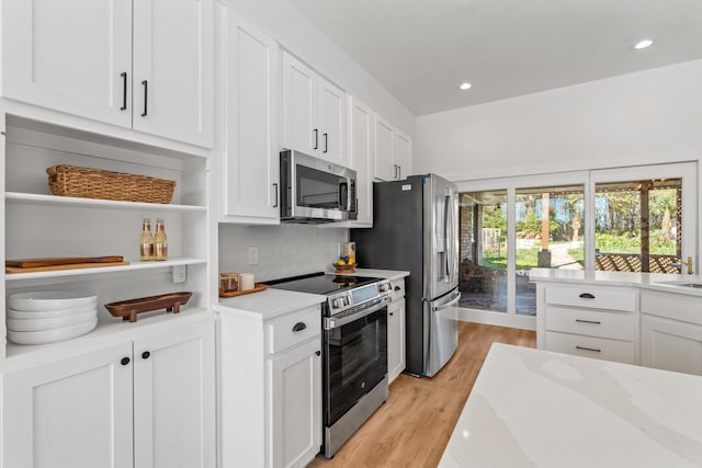 kitchen featuring white cabinets, light wood-type flooring, tasteful backsplash, light stone counters, and stainless steel appliances