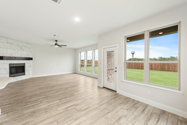 unfurnished living room with a fireplace, light wood finished floors, visible vents, a ceiling fan, and baseboards