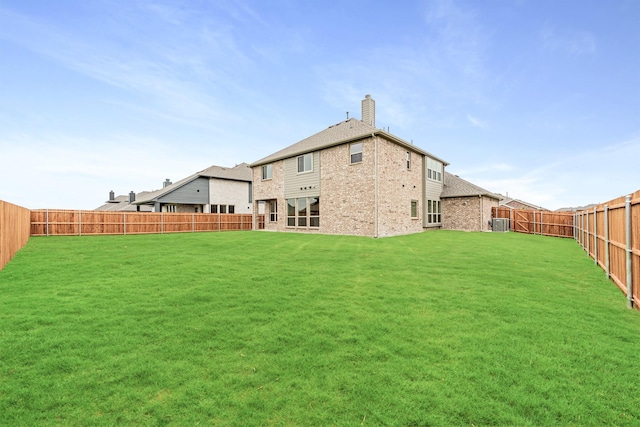 back of house with central AC unit, a fenced backyard, brick siding, a lawn, and a chimney