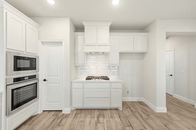 kitchen with white cabinets, light wood-type flooring, tasteful backsplash, and stainless steel appliances