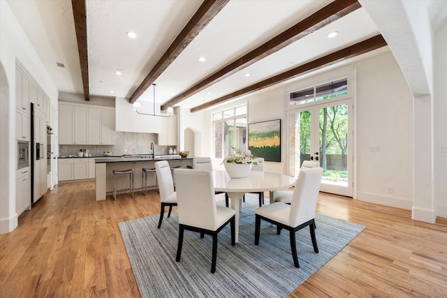 dining area with beam ceiling, light hardwood / wood-style floors, french doors, and sink