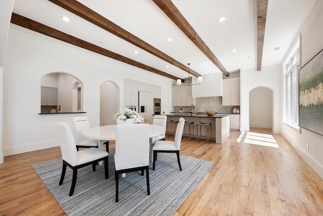 dining area with sink, light wood-type flooring, and beam ceiling