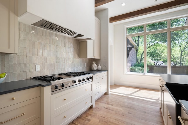 kitchen with tasteful backsplash, stainless steel gas stovetop, beam ceiling, custom range hood, and light hardwood / wood-style flooring