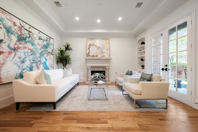 living room with light wood-type flooring, a raised ceiling, ornamental molding, and french doors