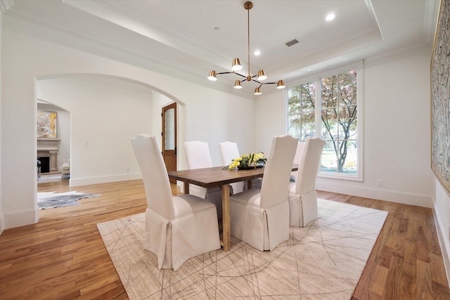 dining space with a notable chandelier, light wood-type flooring, crown molding, and a raised ceiling