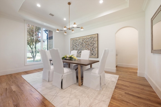 dining space with light wood-type flooring, a raised ceiling, and a notable chandelier