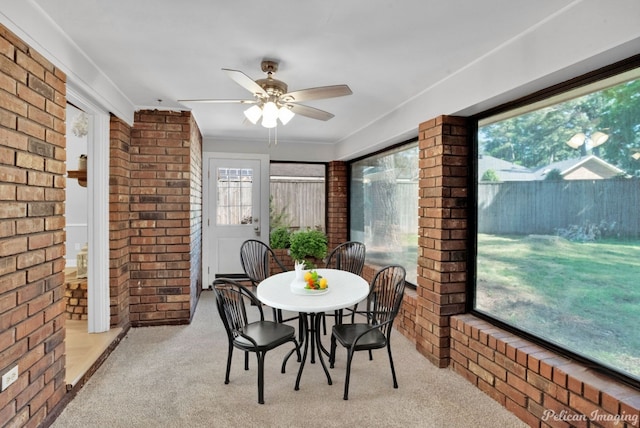 dining room with brick wall, light colored carpet, and ceiling fan