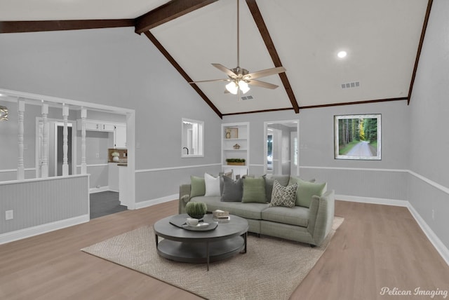 living room with built in features, high vaulted ceiling, beamed ceiling, ceiling fan, and light wood-type flooring