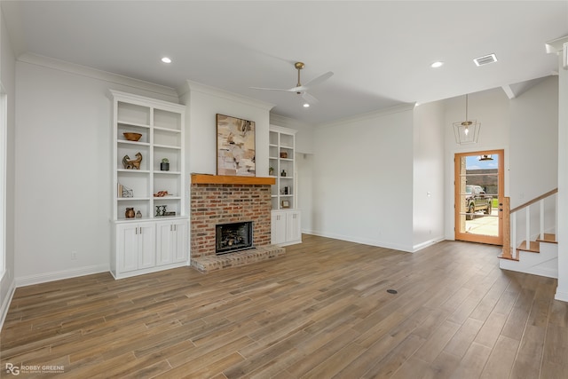 living room featuring hardwood / wood-style flooring, crown molding, built in shelves, a brick fireplace, and ceiling fan