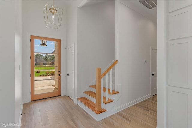 foyer entrance featuring visible vents, baseboards, light wood-style flooring, a high ceiling, and stairs