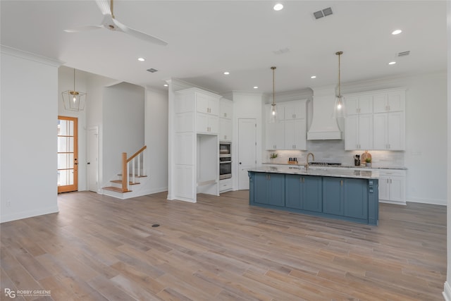 kitchen featuring white cabinets, decorative backsplash, an island with sink, and custom range hood