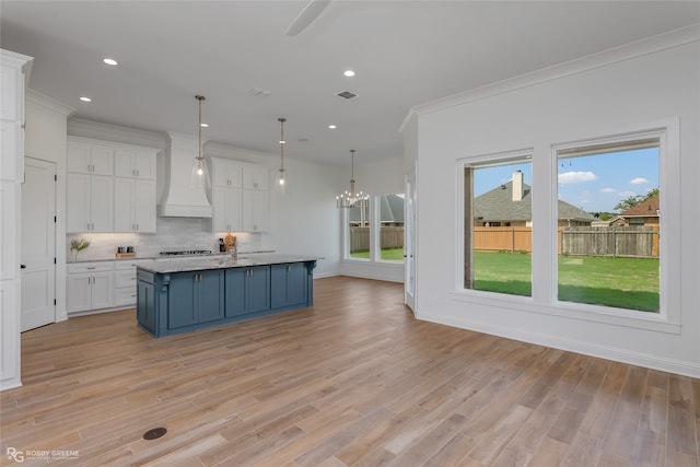 kitchen with decorative backsplash, a healthy amount of sunlight, white cabinets, and custom range hood