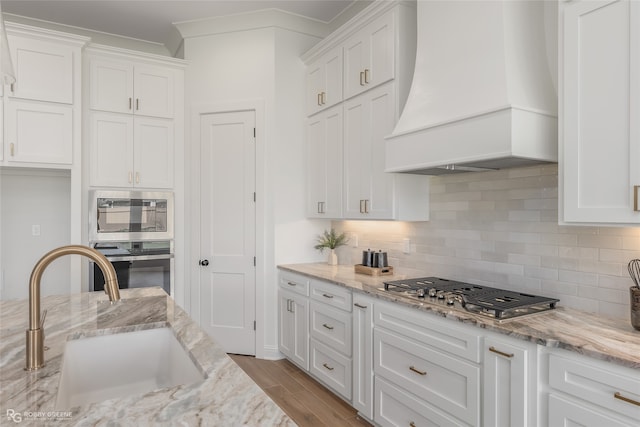 kitchen featuring custom range hood, light hardwood / wood-style flooring, stainless steel appliances, decorative backsplash, and sink