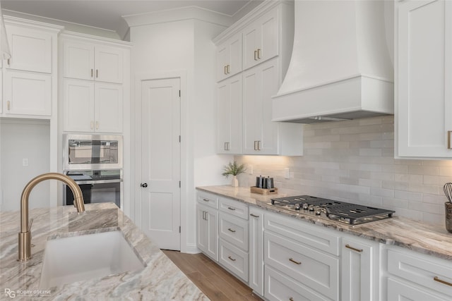 kitchen featuring white cabinets, decorative backsplash, custom range hood, stainless steel appliances, and a sink