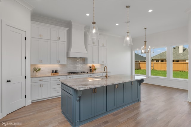 kitchen featuring white cabinets, stainless steel gas stovetop, sink, custom range hood, and backsplash