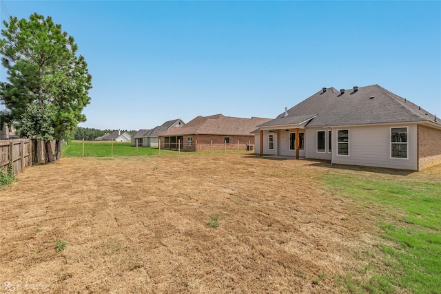 back of house featuring roof with shingles, a lawn, and a fenced backyard