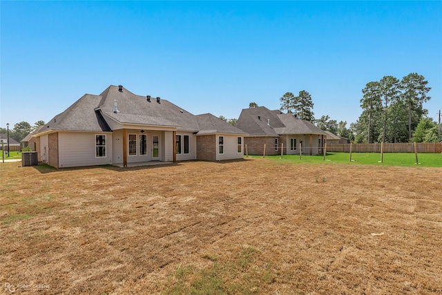 back of property with central AC unit, a lawn, fence, and brick siding