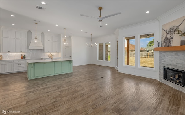 kitchen featuring hardwood / wood-style floors, a stone fireplace, premium range hood, backsplash, and a kitchen island with sink