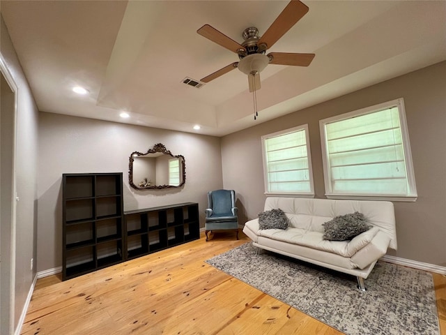 sitting room with ceiling fan, light hardwood / wood-style flooring, and a tray ceiling