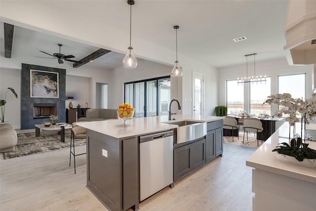 kitchen featuring pendant lighting, stainless steel dishwasher, a kitchen island with sink, and sink