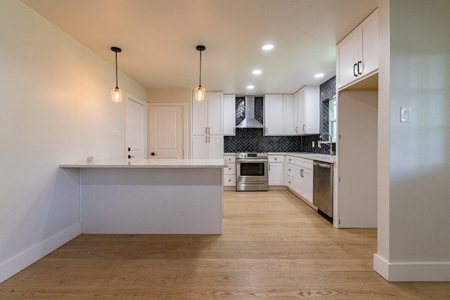 kitchen with light hardwood / wood-style floors, decorative light fixtures, wall chimney exhaust hood, appliances with stainless steel finishes, and white cabinetry