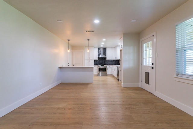 kitchen with white cabinetry, stainless steel appliances, light hardwood / wood-style flooring, wall chimney exhaust hood, and hanging light fixtures