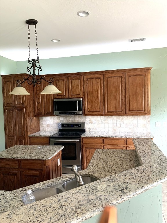 kitchen with light stone countertops, appliances with stainless steel finishes, tasteful backsplash, sink, and pendant lighting