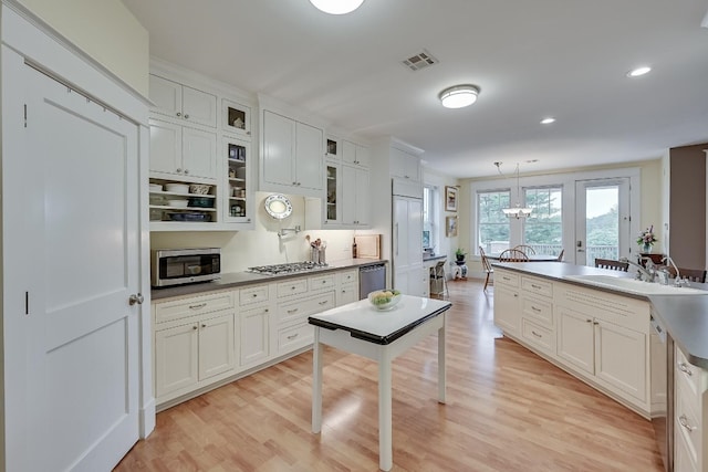 kitchen featuring appliances with stainless steel finishes, light hardwood / wood-style floors, hanging light fixtures, and white cabinetry