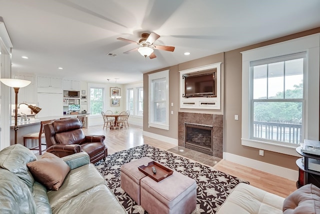 living room with a fireplace, a wealth of natural light, ceiling fan, and light hardwood / wood-style floors