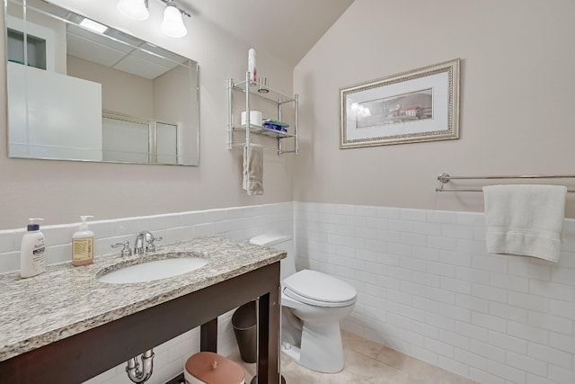 bathroom featuring tile walls, vaulted ceiling, toilet, tile flooring, and vanity