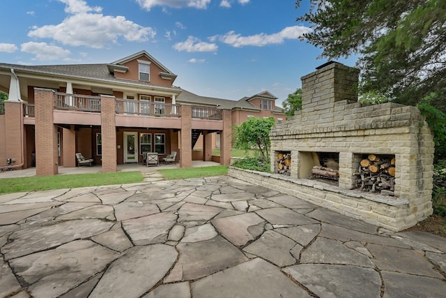 back of property featuring an outdoor brick fireplace and a patio area