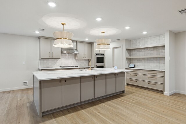 kitchen featuring gray cabinetry, stainless steel appliances, hanging light fixtures, light hardwood / wood-style floors, and a kitchen island with sink